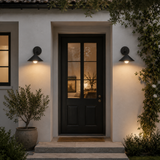 Dark wooden front door of a house with wall lights on either side, illuminated by warm lighting.