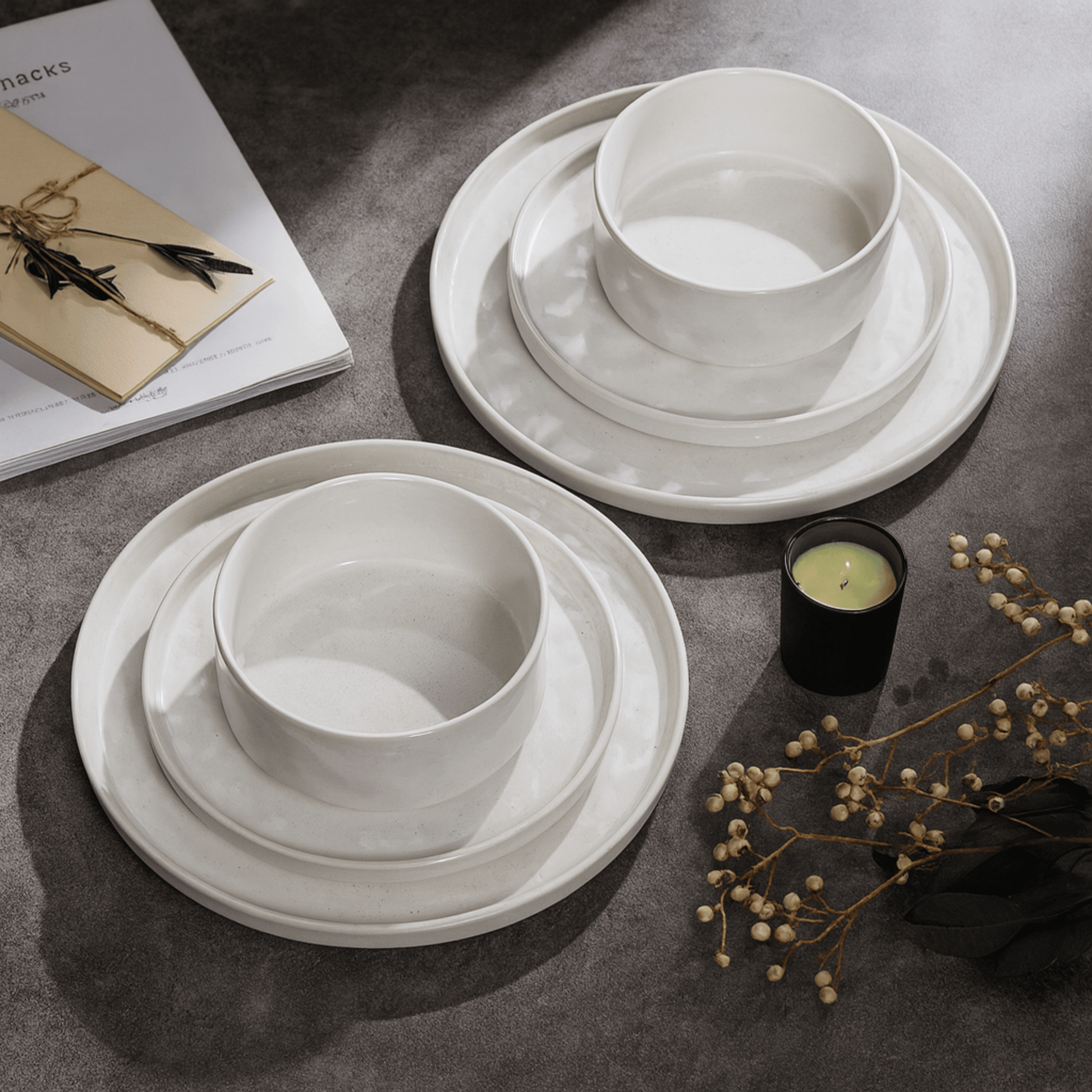 White ceramic bowls and plates on a dark surface with a candle and dried flowers.