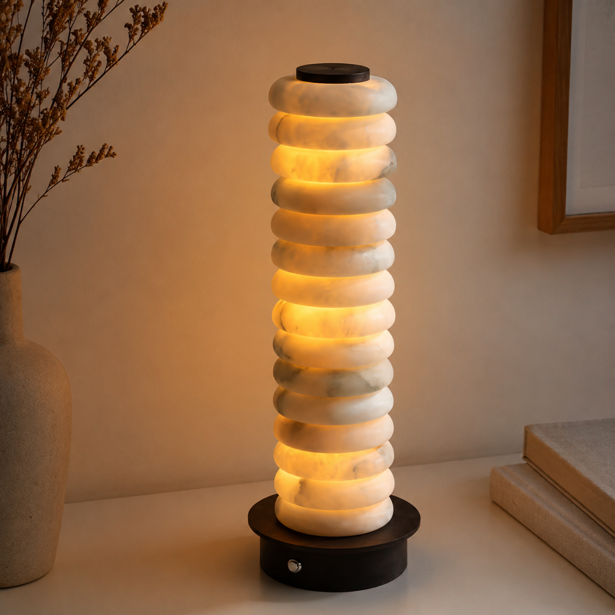 Decorative lamp with stacked circular design on a surface, with a vase and books in the background.