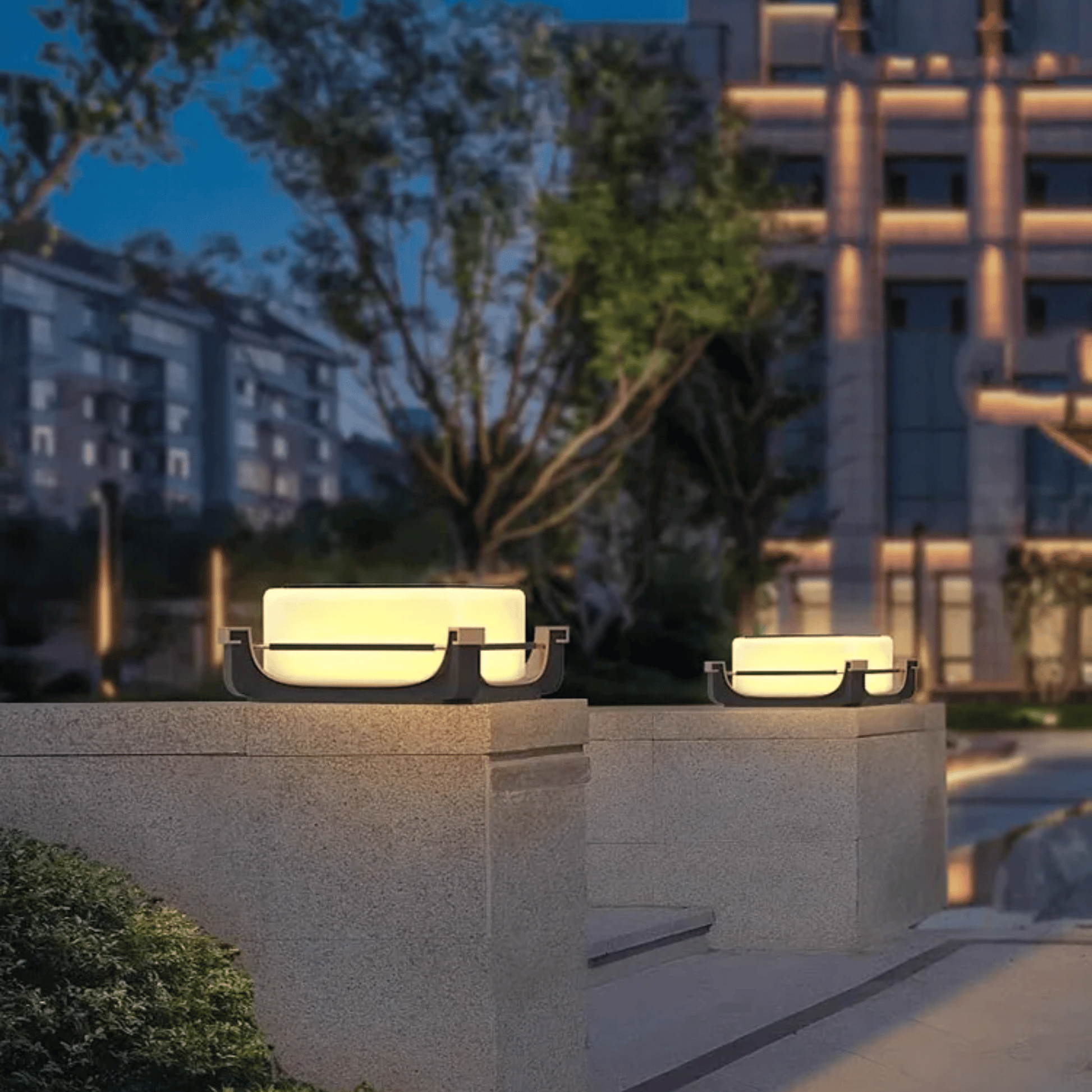Two outdoor lights on stone plinths with a blurred building and tree in the background.