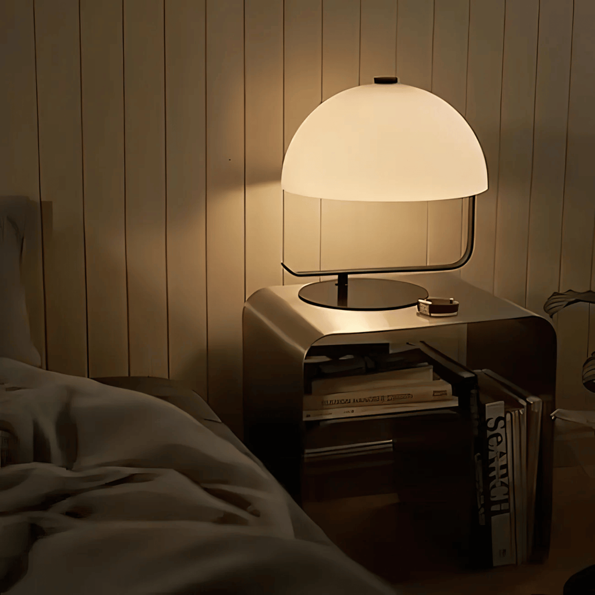 Table lamp on a nightstand next to a bed with books underneath, in a dimly lit room.