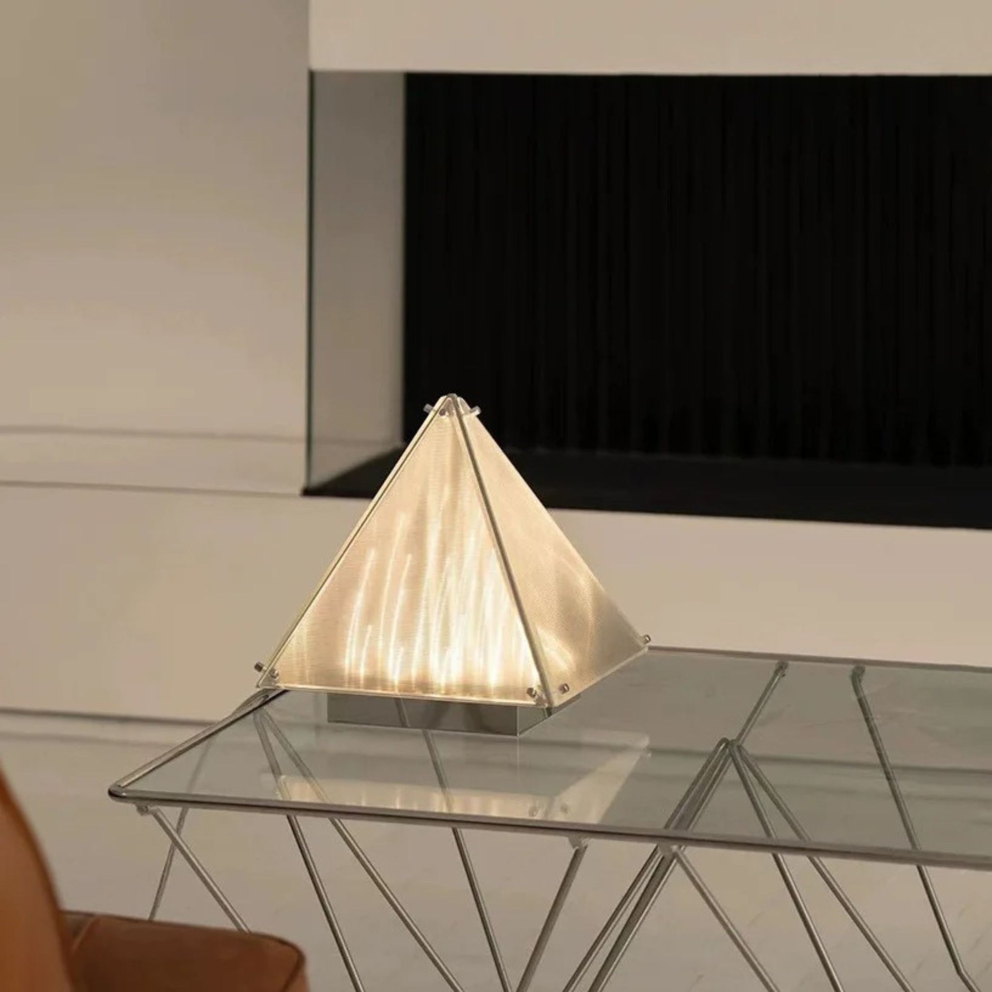 A cone-shaped table lamp with pleated translucent sides, glowing warmly on a glass-top table in a modern interior.