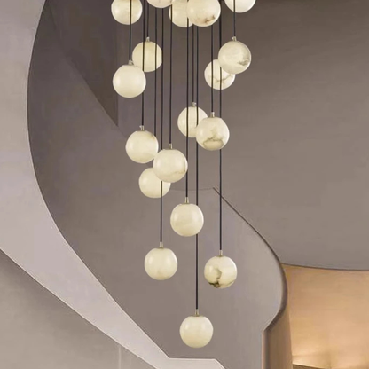 A tall chandelier with multiple glowing globe lights hanging in a spiral formation inside a modern staircase area.