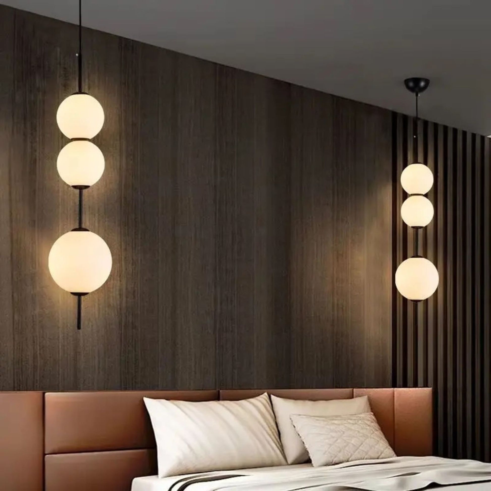 A modern pendant light with three large globe bulbs hanging in a vertical line above a bed in a stylish bedroom.