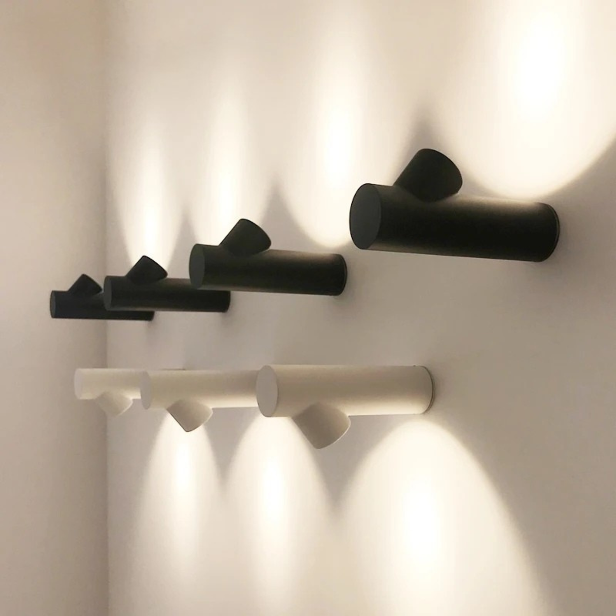 	
A modern black wall lamp casts warm light onto a textured, grayish wall above a small cactus plant and a gray cushion, creating a cozy and stylish atmosphere.