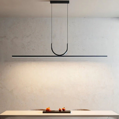 A minimalist black pendant light with a linear design, casting soft light on a beige wall above a countertop.