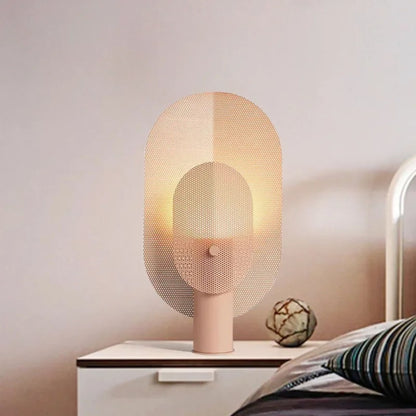 A modern table lamp with a soft pink base and a woven mesh shade, casting a warm glow on a bedside table.