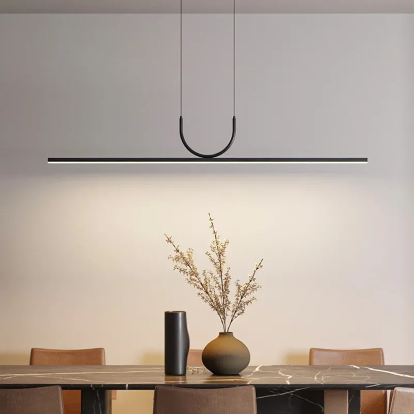 Modern minimalist dining area with a slim black pendant light hanging above a wooden table decorated with a vase of dried plants