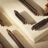Modern bronze and wood cabinet handles displayed on a light beige background with warm lighting