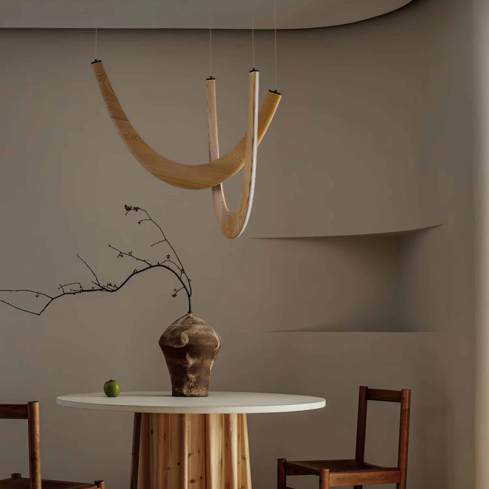 A unique pendant light with two curved wooden arms hanging above a round dining table in a minimalist setting.