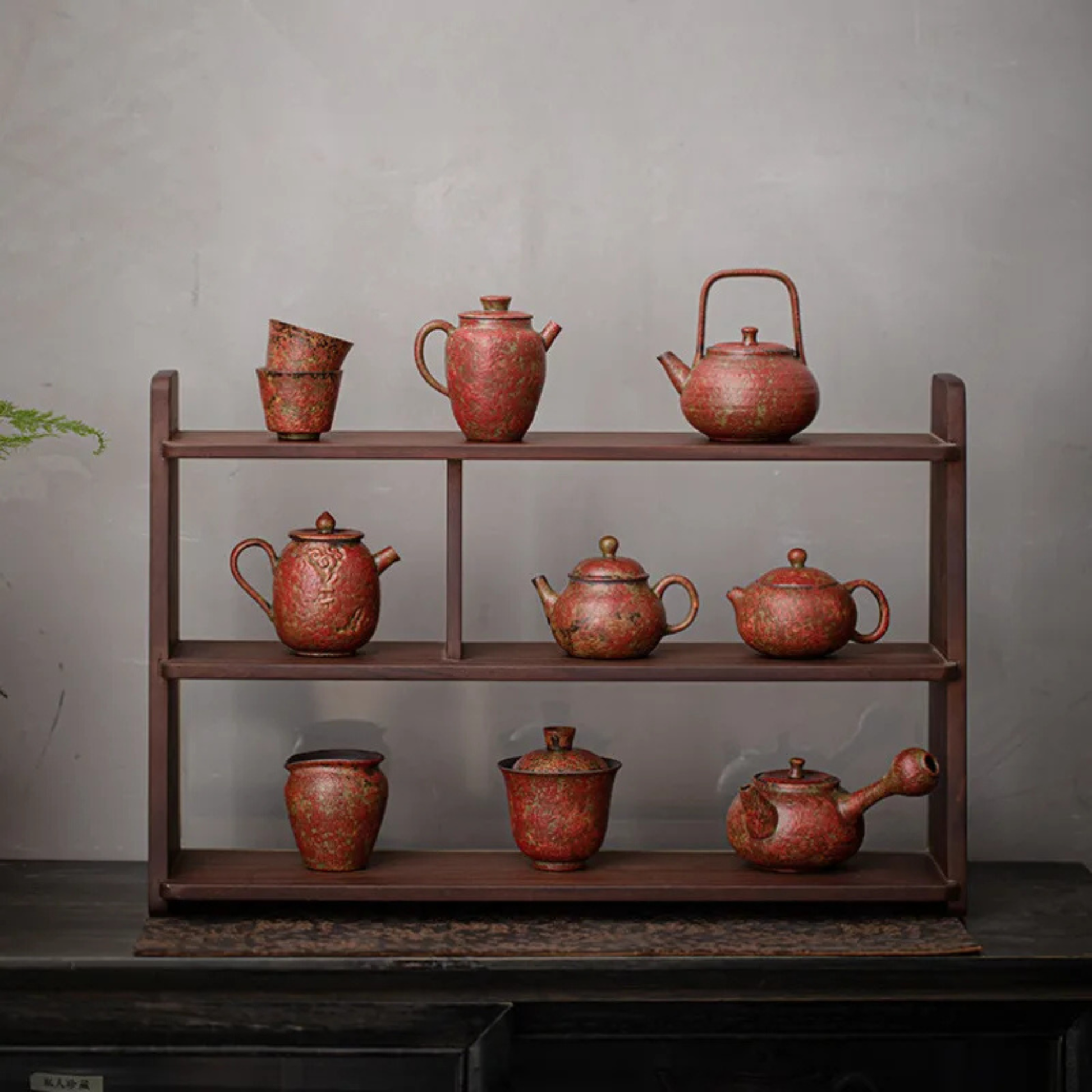A wooden display shelf holding a full set of red, textured ceramic teapots, cups, and jars arranged neatly against a gray wall.