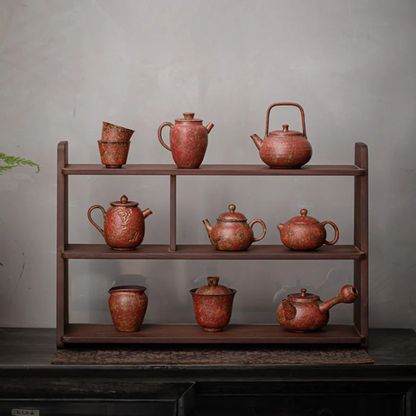 A wooden display shelf holding a full set of red, textured ceramic teapots, cups, and jars arranged neatly against a gray wall.