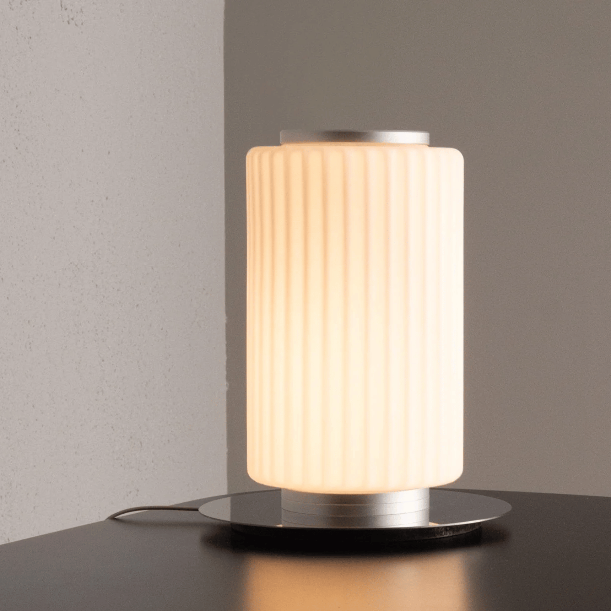 Table lamp with ribbed design on a dark surface against a gray wall