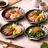 Four plates of Japanese cuisine on a light stone surface with chopsticks and wasabi.
