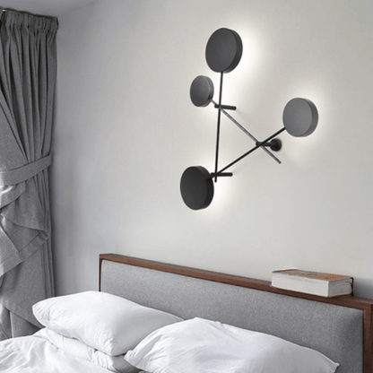 Modern wall lamp with circular design on a white wall above a bed.