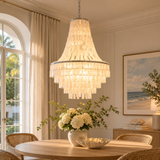 Chandelier hanging above a dining table with a vase of flowers in a room with large windows and a painting on the wall.