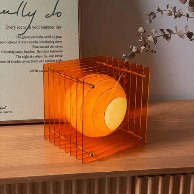 Orange cylindrical lamp with transparent cage on a wooden surface