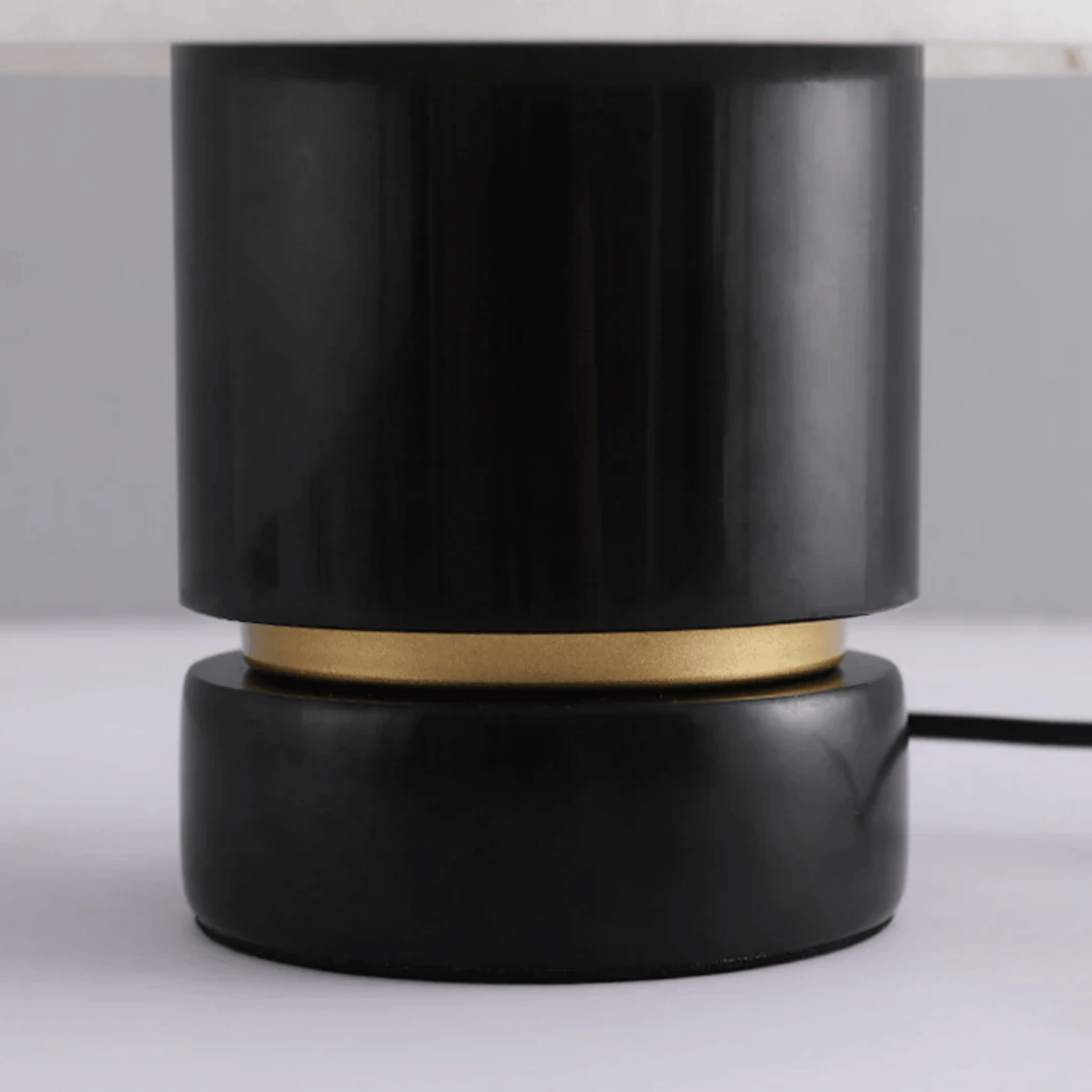 Black cylindrical lamp with gold accent on a white surface