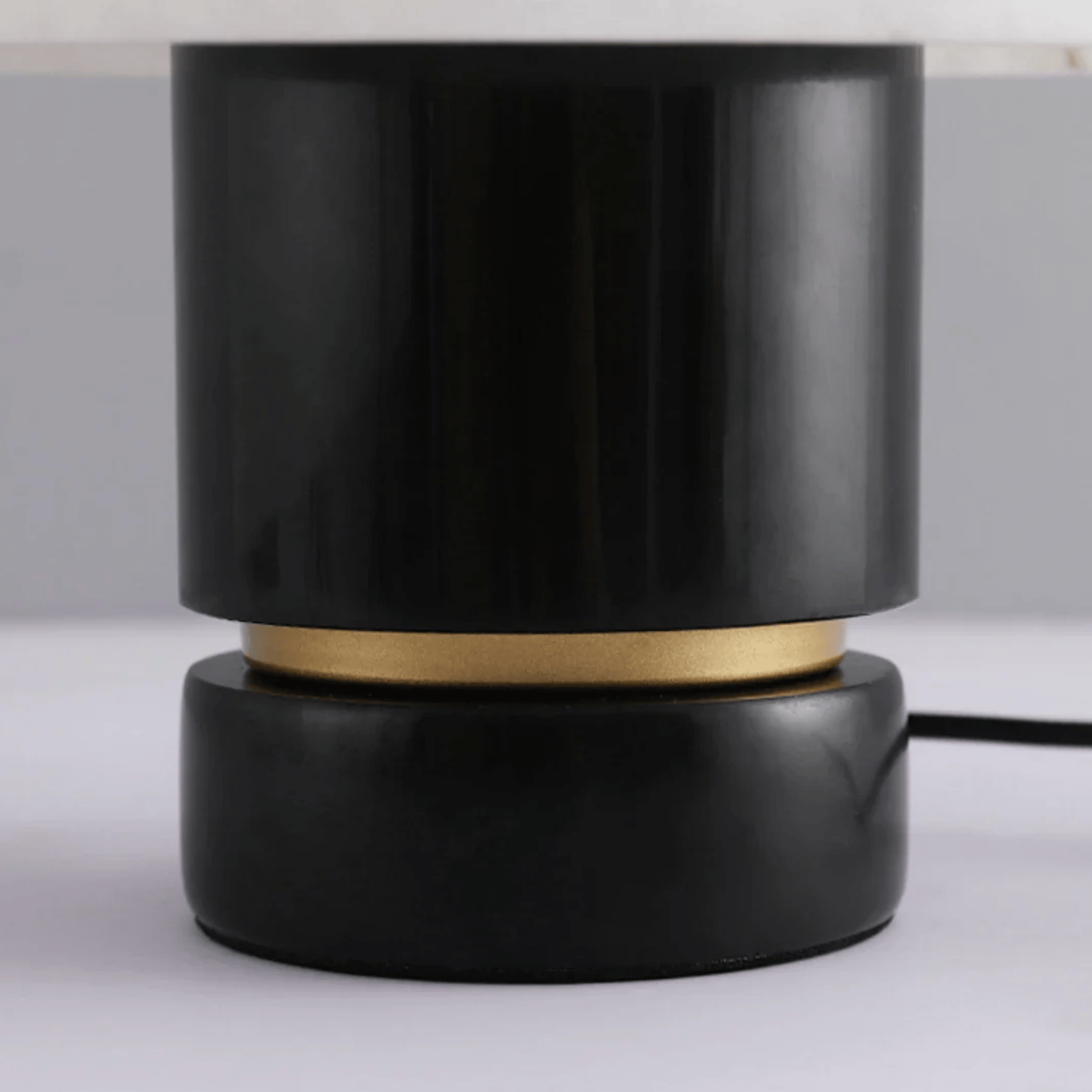 Black cylindrical lamp with gold accent on a white surface