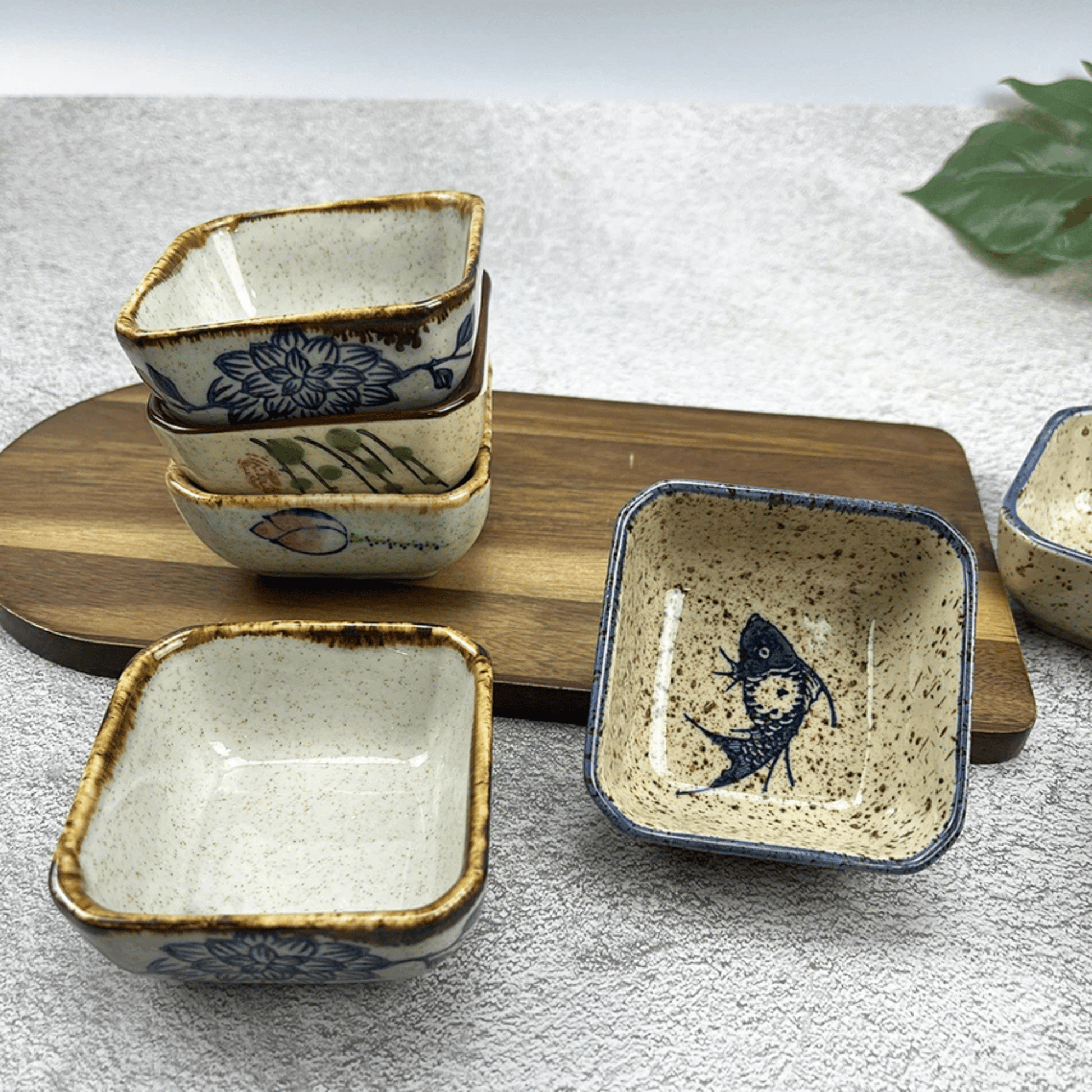 Set of square ceramic dishes with decorative patterns on a wooden board.
