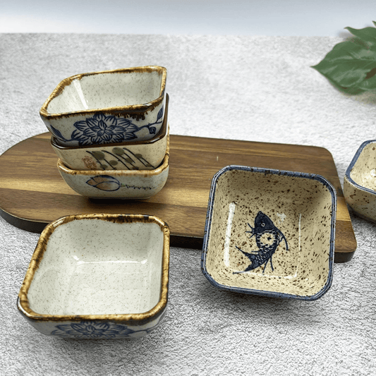 Set of square ceramic dishes with decorative patterns on a wooden board.