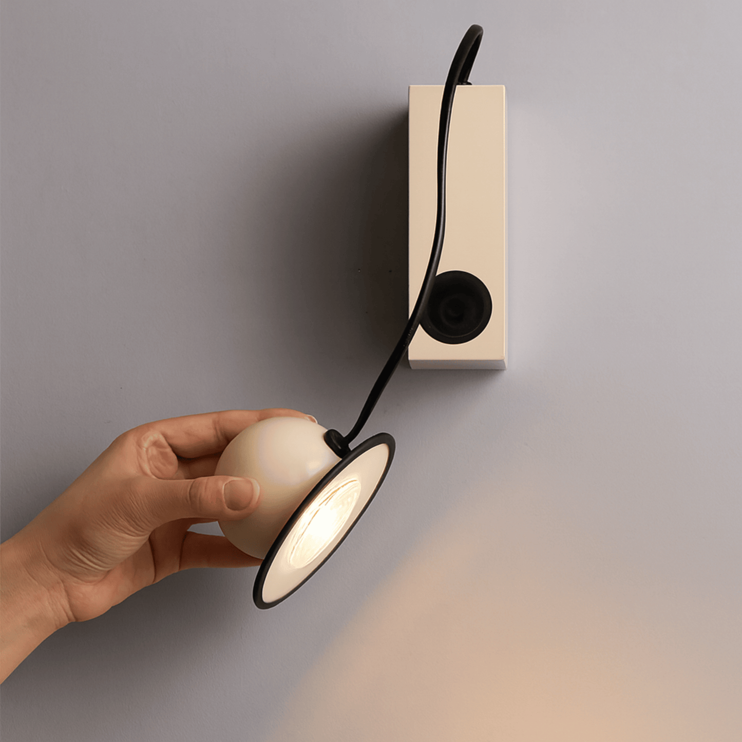 Hand adjusting a wall-mounted light fixture with a neutral background