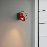 Red wall light fixture on a gray wall with a black metal ladder in the background