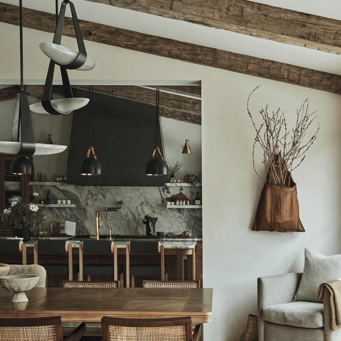 Modern kitchen with wooden dining table and chairs, pendant lights, and a vase with branches on the wall.