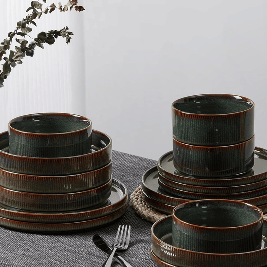 Set of green ceramic dinnerware with brown rim on a gray surface.
