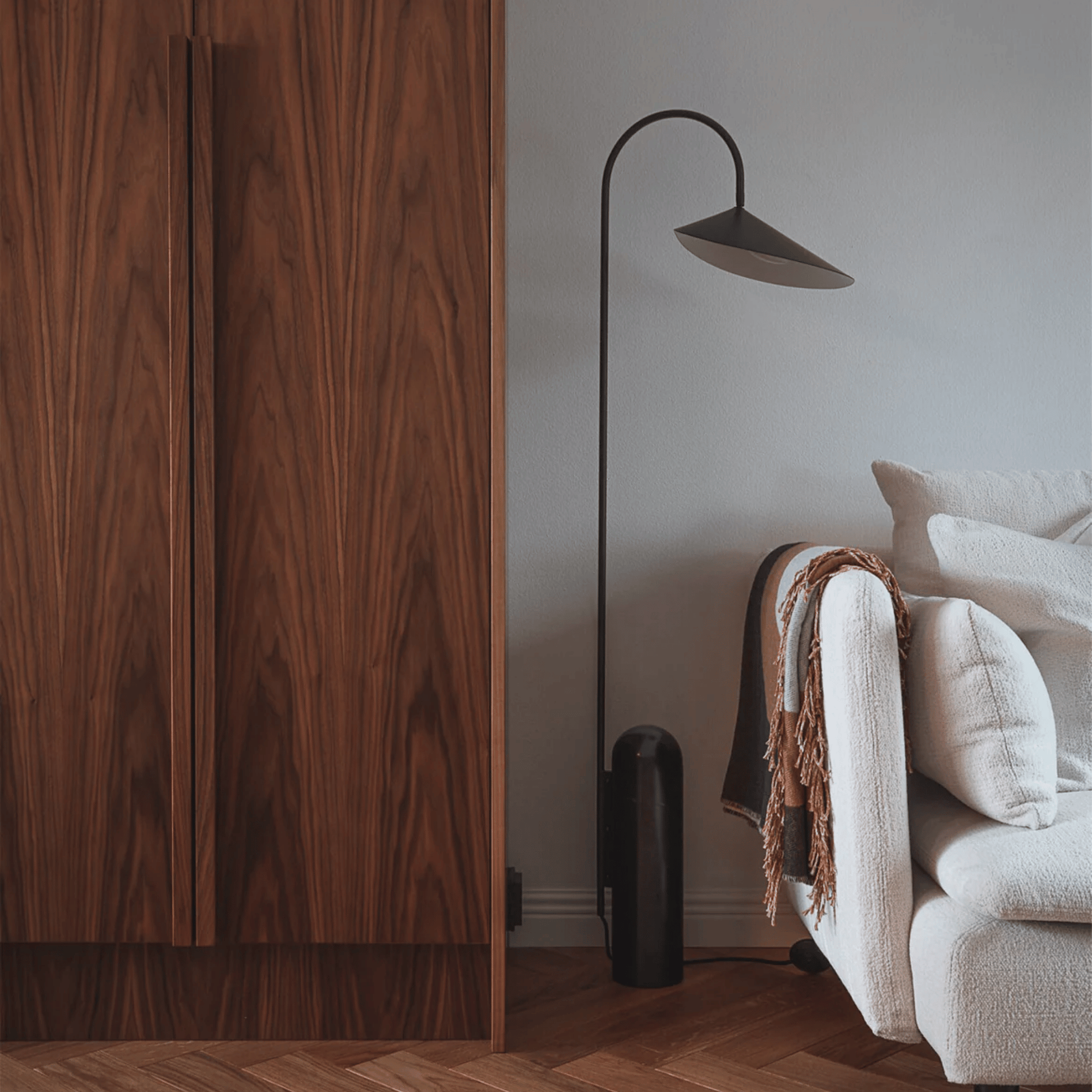 Wooden wardrobe next to a white sofa with a blanket and a black floor lamp in a room.
