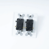 Two black electrical switches on a clear plastic base against a white background