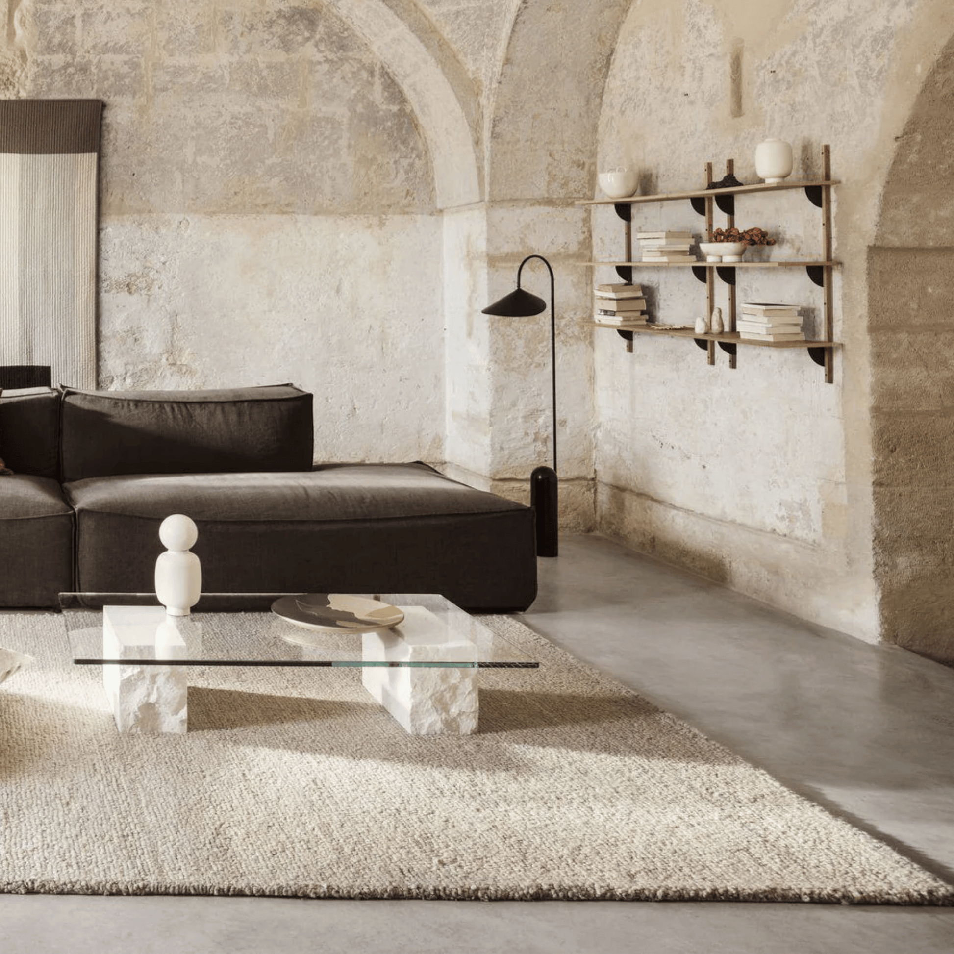 Modern living room with a black sofa, glass coffee table, and shelves against a textured wall.