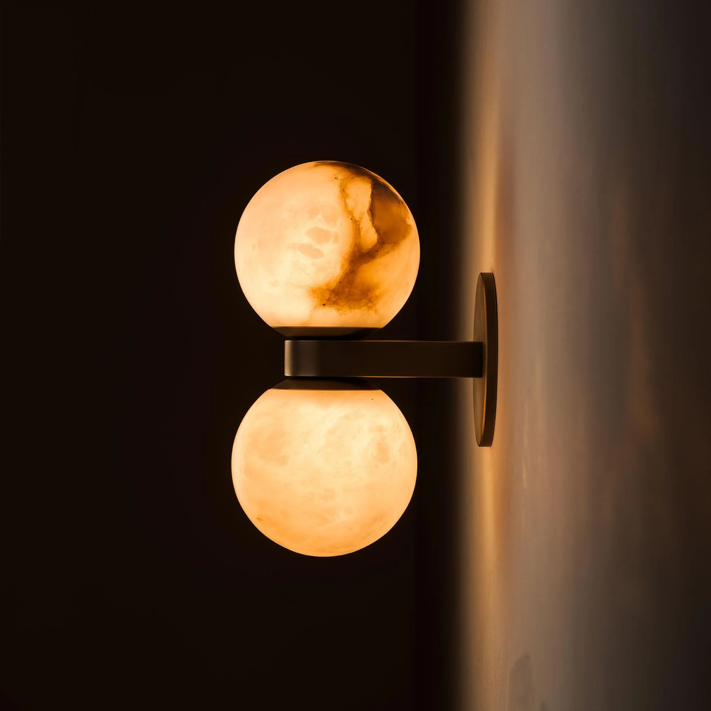 Wall-mounted double spherical light fixture casting a warm glow on a dark wall.