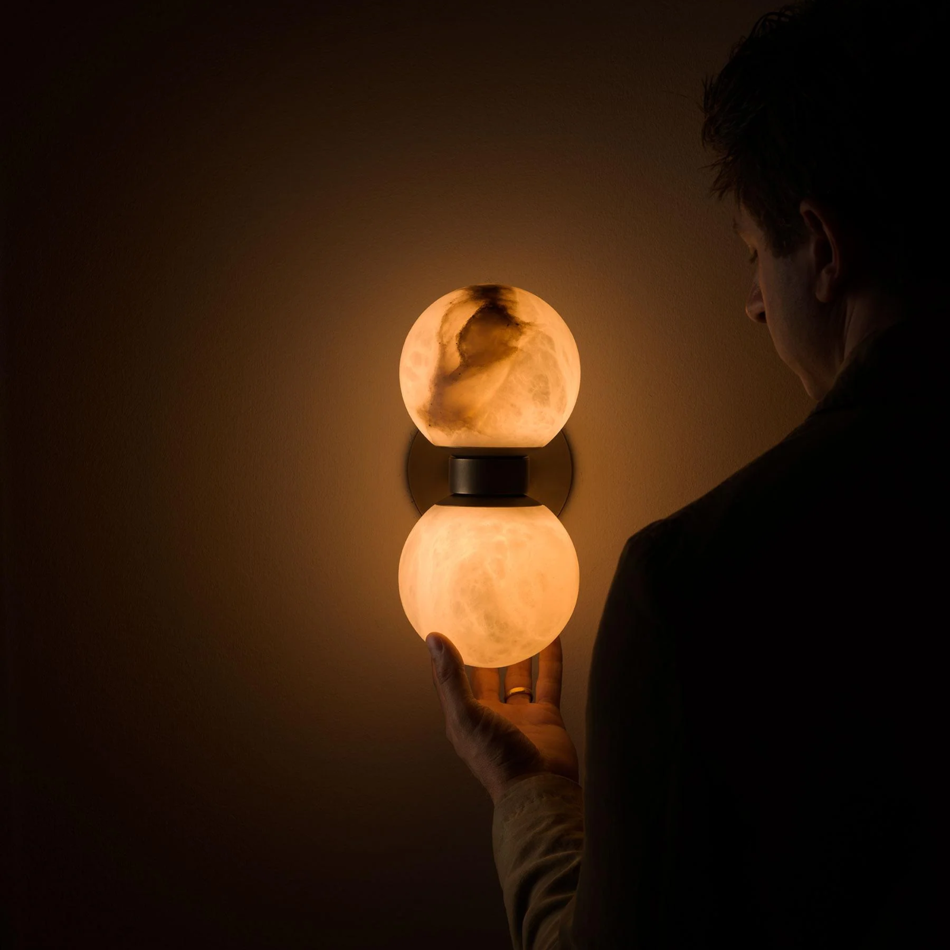 Person interacting with a wall-mounted lamp in a dimly lit room
