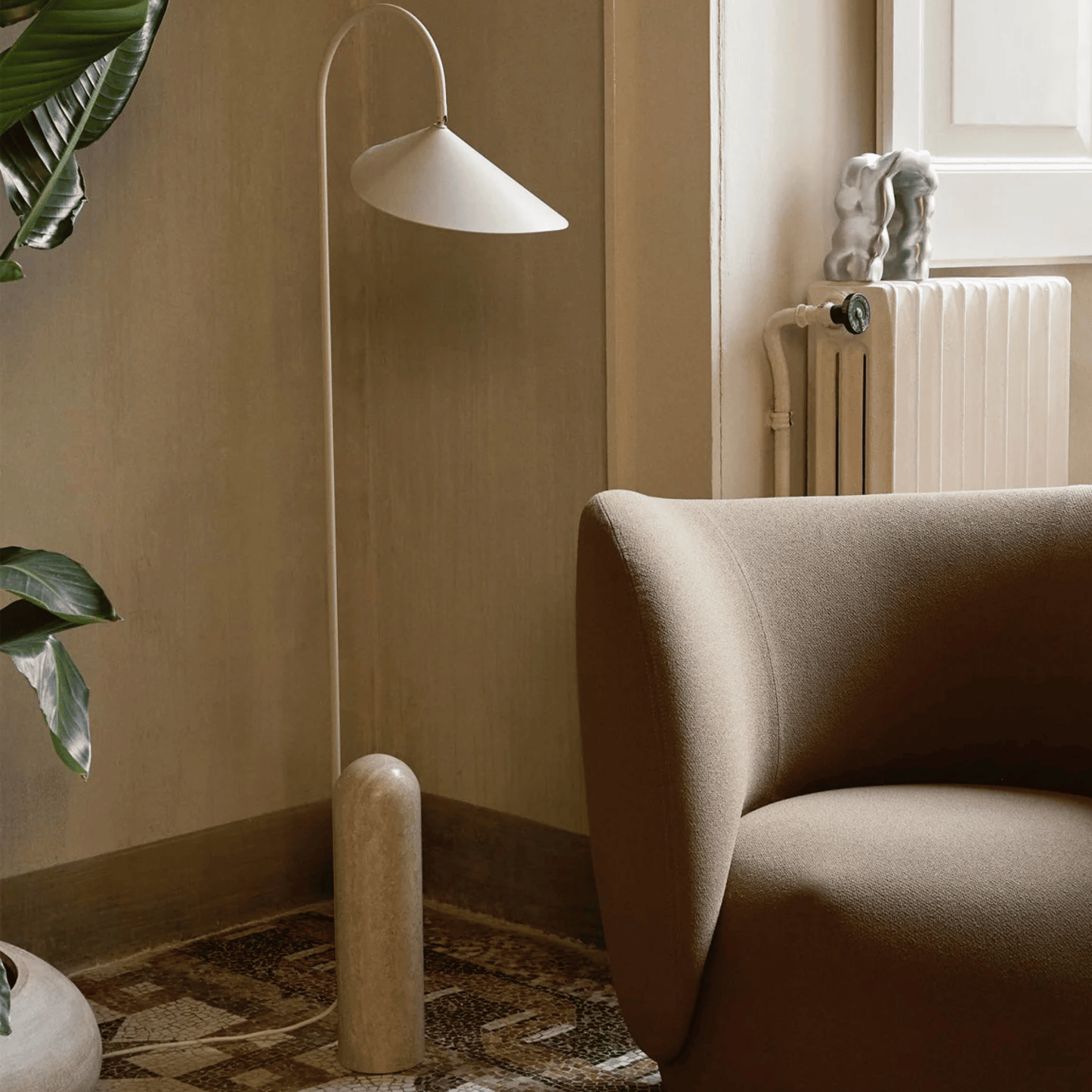 Modern floor lamp next to a beige armchair in a room with a radiator and plant.