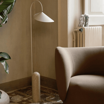 Modern floor lamp next to a beige armchair in a room with a radiator and plant.