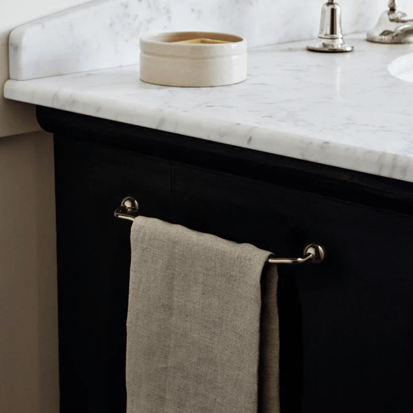 Bathroom vanity with marble countertop, towel hanging on rack, and decorative bowl.