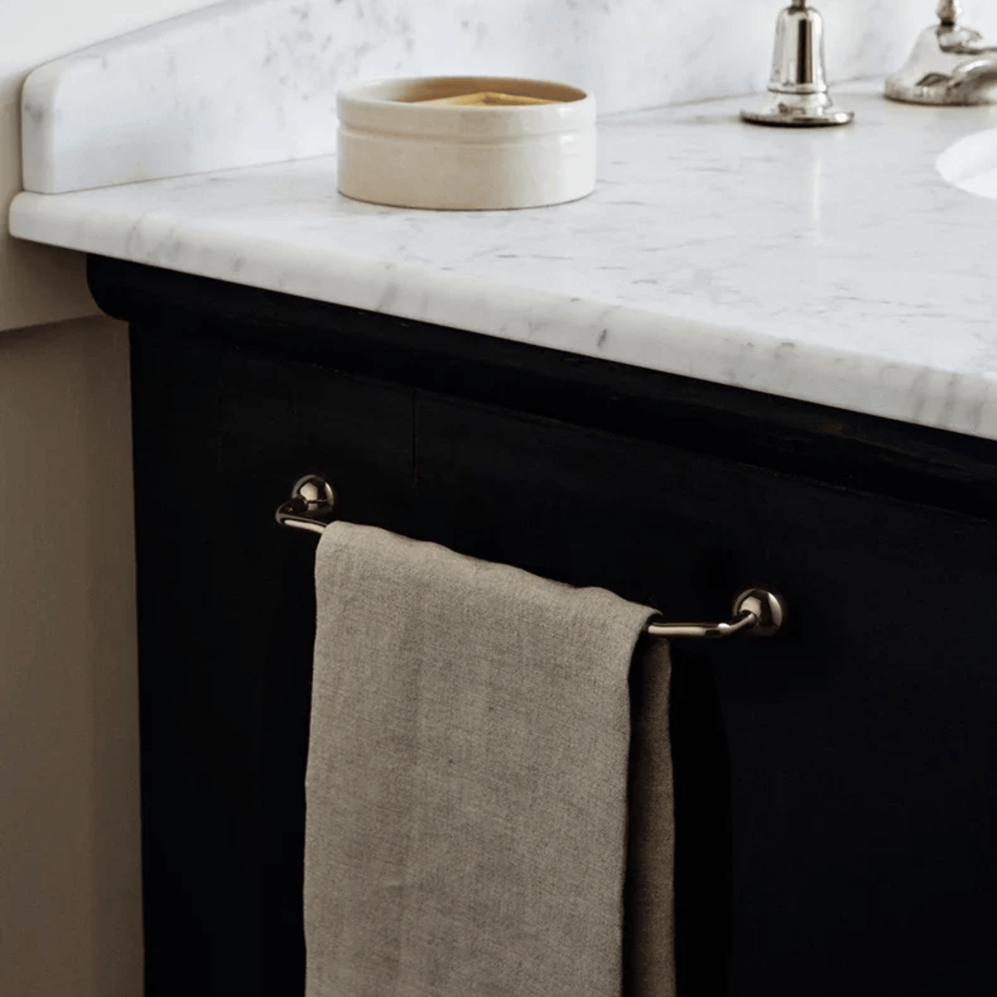 Bathroom vanity with marble countertop, towel hanging on rack, and decorative bowl.