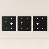 Three black wall plates with different electrical symbols on a beige background