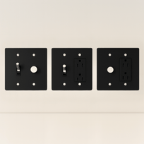 Three black wall plates with different electrical symbols on a beige background