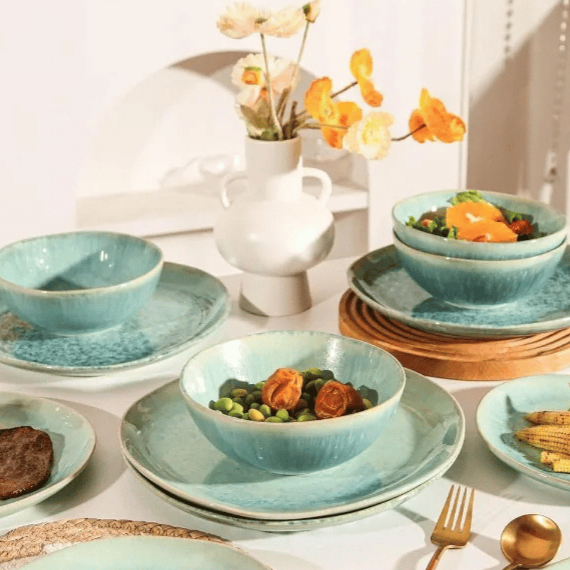 Set of blue ceramic dishes with food on a table with a vase of flowers in the background.