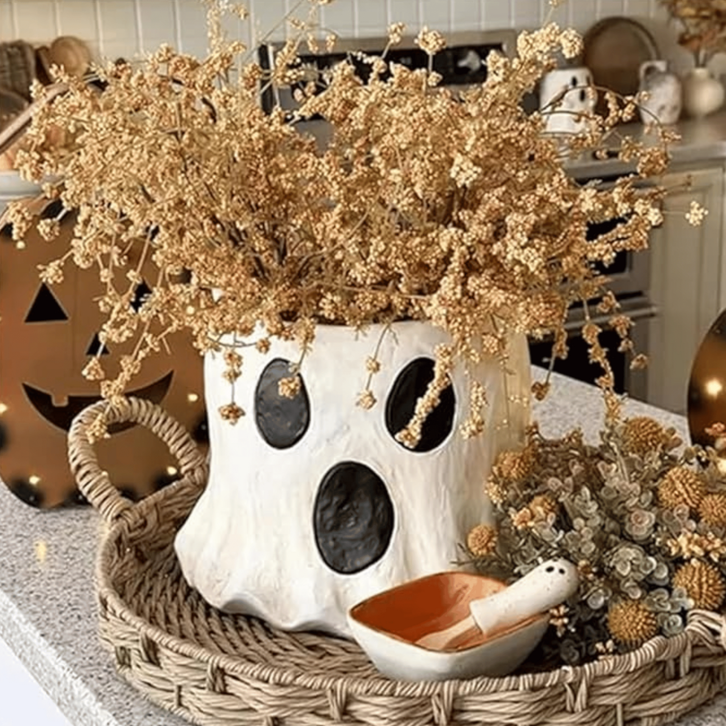Decorative ghost vase with dried flowers on a table with Halloween-themed items.