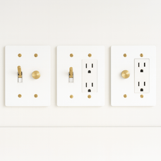 Three white light switch and outlet covers with gold accents on a white background