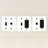 Three white wall plate covers with black outlets on a beige background