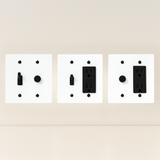 Three white wall plate covers with black outlets on a beige background