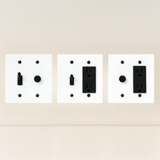 Three white wall plate covers with black outlets on a beige background