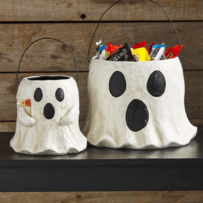 Two ghost-shaped Halloween candy buckets with treats on a wooden background