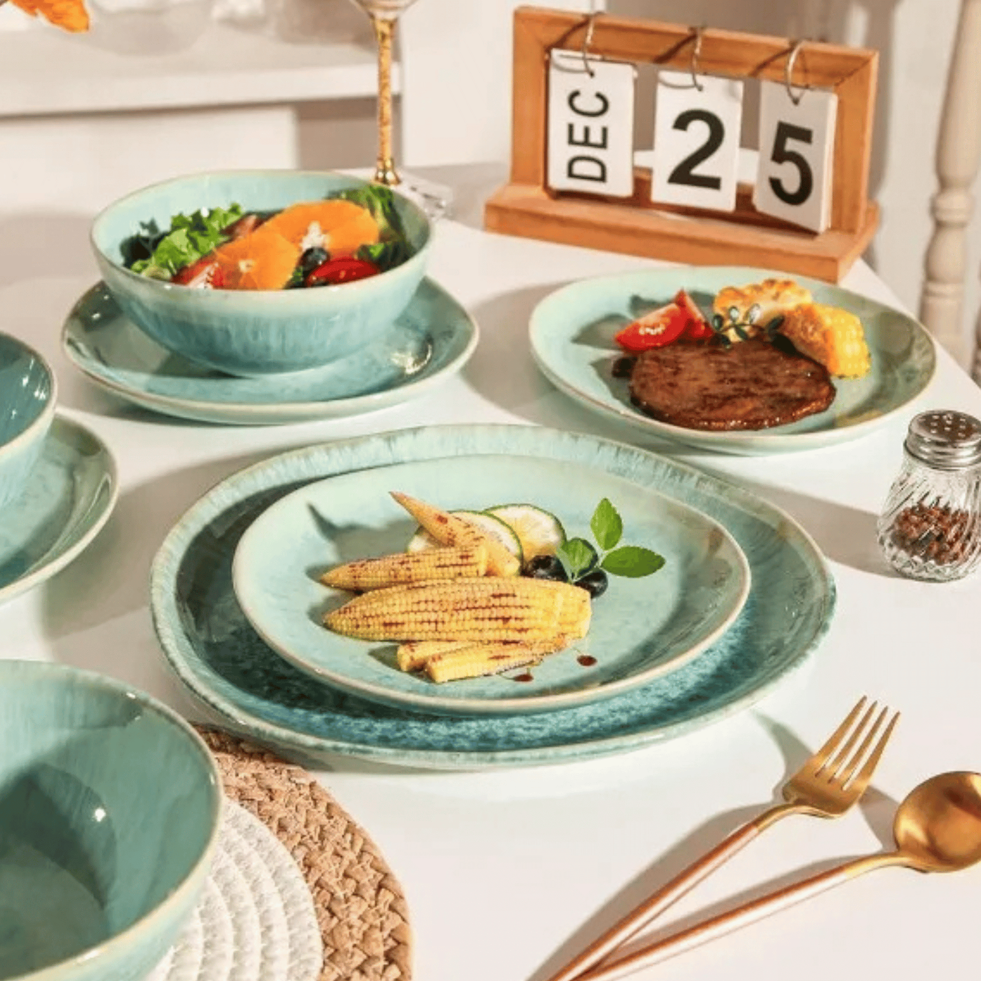 Teal ceramic tableware set with food on a white surface, including plates, bowls, and cutlery.