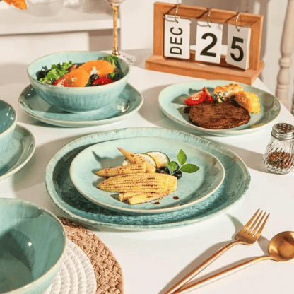Teal ceramic tableware set with food on a white surface, including plates, bowls, and cutlery.