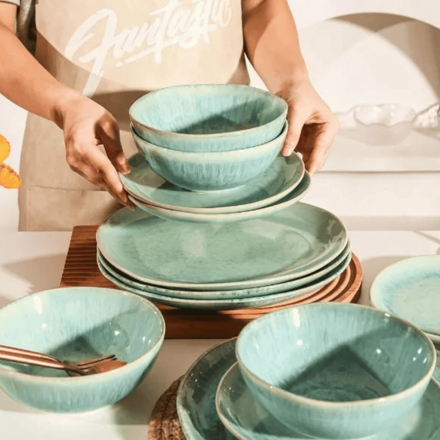 Person holding a stack of teal ceramic dishes on a table.